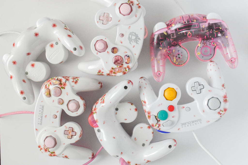 grouping of several customized nintendo gamecube controllers, all of varying floral cherry blossom designs