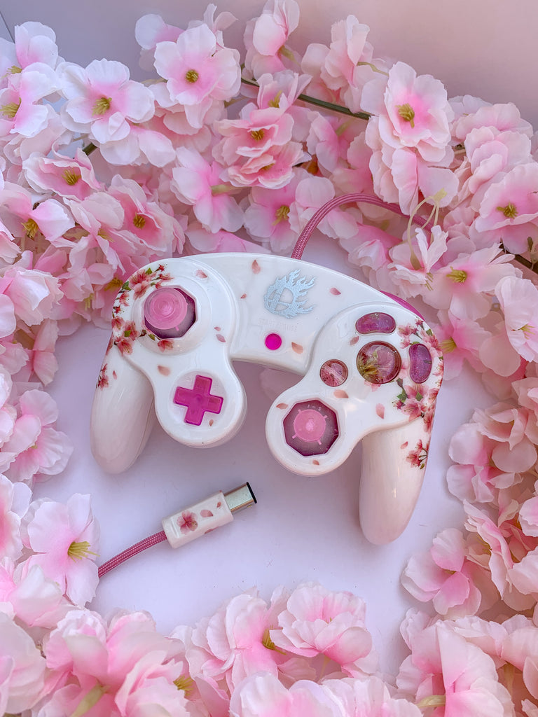 custom nintendo gamecube controller with a pink floral cherry blossom design surrounded by artificial cherry blossom flowers #customgcc #customgamecubecontroller #customcontroller #customgamecube