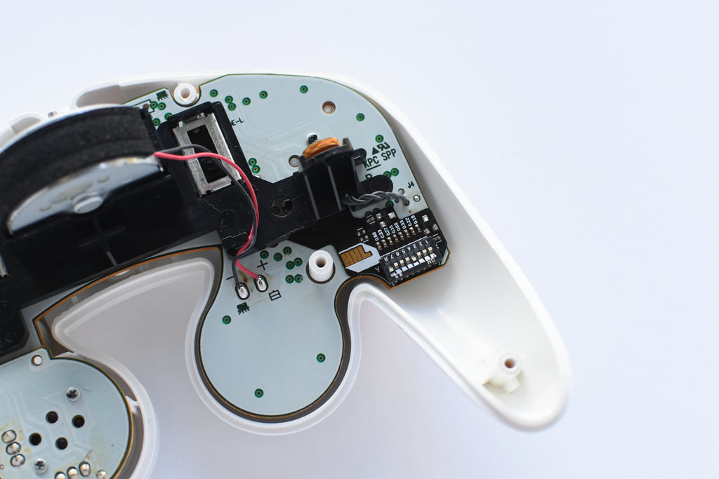image of an opened up gamecube controller showing back of motherboard. there is a flat black module inserted underneath the black housing